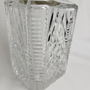 K&ouml;nnte beinhalten: Eine klare, facettierte Glasparf&uuml;mflasche mit silberfarbenem Deckel. Die Flasche hat ein geometrisches Design mit abgewinkelten Schnitten und eine rechteckige Form. Der Deckel ist aus glattem, metallischem Material. Die Flasche ist leer und steht vor wei&szlig;em Hintergrund.