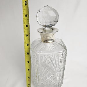 K&ouml;nnte beinhalten: Eine klare Glas-Dekantierkaraffe mit einem facettierten Kristallverschluss und einem silberfarbenen Kragen. Die Karaffe ist etwa 25 cm hoch. Der K&ouml;rper weist ein Diamant- und F&auml;chermuster auf.