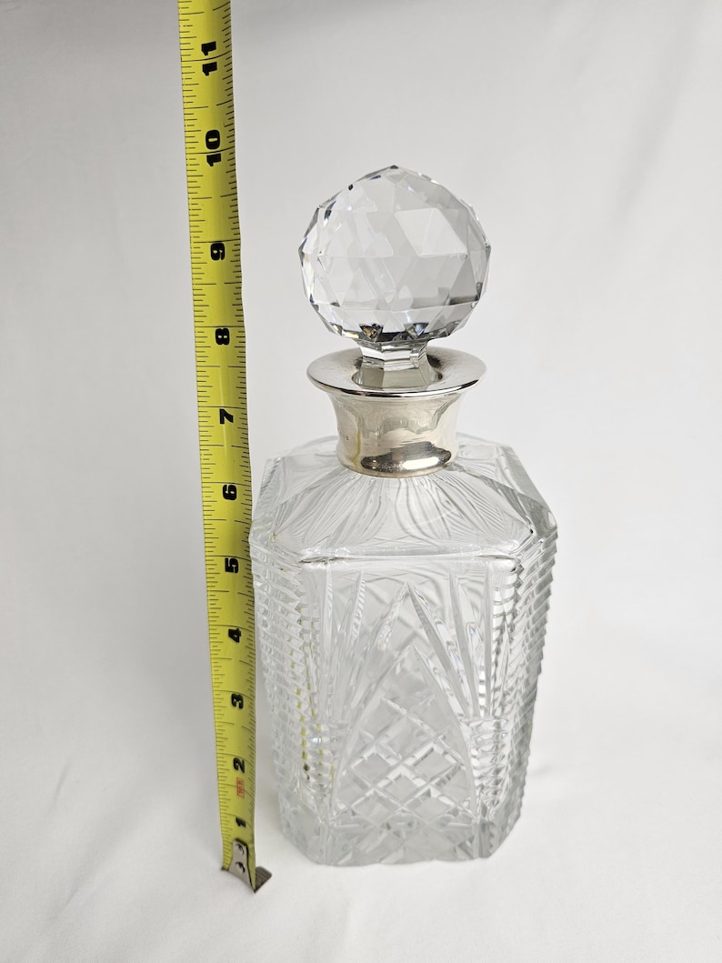 K&ouml;nnte beinhalten: Eine klare Glas-Dekantierkaraffe mit einem facettierten Kristallverschluss und einem silberfarbenen Kragen. Die Karaffe ist etwa 25 cm hoch. Der K&ouml;rper weist ein Diamant- und F&auml;chermuster auf.