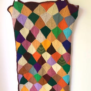 May include: A rectangular knitted blanket featuring a repeating diamond pattern in a vibrant array of colours including orange, green, purple, brown, yellow, blue, pink, and cream. The edges are finished with a dark brown crocheted border.