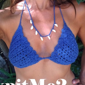 Op de afbeelding: Een blauwe gehaakte bikini top met een witte schelpenketting. De bikini top heeft een gegolfde rand en een delicaat haakpatroon.