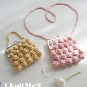 Puede incluir: Dos monederos de ganchillo, uno rosa y otro amarillo, con cierre de broche metálico. El monedero rosa tiene una correa larga, mientras que el monedero amarillo tiene un asa más corta. Los monederos están sobre una superficie blanca con una flor blanca y pétalos.