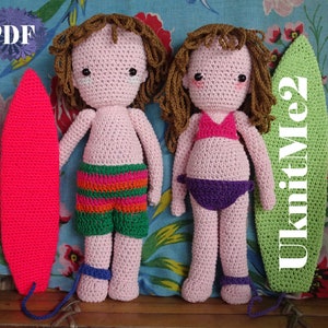 Può includere: Due bambole all'uncinetto vestite con costumi da bagno che tengono in mano delle tavole da surf. La bambola a sinistra indossa pantaloncini da bagno a righe verdi e arancioni e tiene una tavola da surf rosa. La bambola a destra indossa un bikini rosa e tiene una tavola da surf verde con la scritta "KnitMe2" sopra.