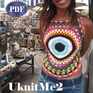 May include: A colorful crochet top with a large, black eye design. The top is sleeveless and has a loose fit. The eye design is surrounded by a rainbow of colors, including pink, orange, yellow, green, blue, and purple.