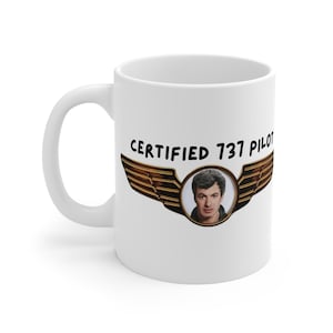 Pode incluir: Caneca de cerâmica branca com uma alça. O design inclui o texto "CERTIFIED 737 PILOT" acima de uma imagem circular de uma pessoa e um par de asas douradas.