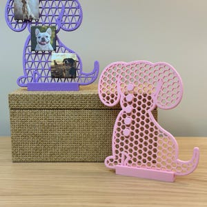 May include: Two dog-shaped photo frames. One is purple and holds three small photos of dogs. The other is pink. Both frames have a geometric openwork design and a small base to stand upright.