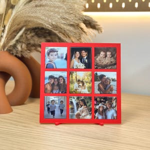 May include: A red square photo frame with nine individual photo slots, each filled with a different family photo. The frame is standing upright on a wooden surface, showcasing various family moments.