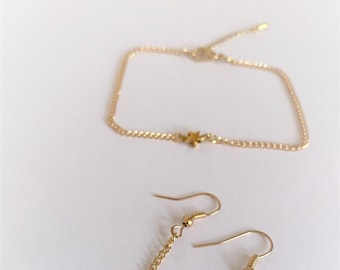 Puede incluir: Un conjunto de joyas doradas que incluye un brazalete delicado de cadena con un dije de estrella y un par de aretes colgantes con dijes de estrella.