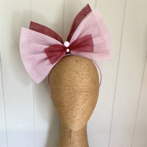 Könnte beinhalten: Ein rosa und burgunderfarbenes Tüll-Haarband mit einem weißen Perlenakzent. Das Haarband befindet sich auf einem braunen Mannequin-Kopf.
