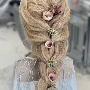 May include: A blonde hairstyle with a braided ponytail decorated with small pink and white flowers.