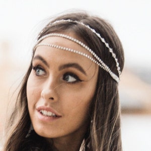 May include: A silver rhinestone headband with three strands. The strands are delicate and sparkle, creating a glamorous accessory. The headband is worn across the forehead and adds a touch of elegance.