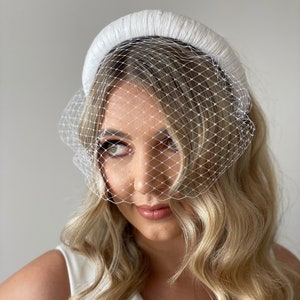 May include: A white padded headband with a white birdcage veil. The veil is made of a fine mesh material.