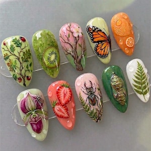 May include: A collection of ten artificial nails with detailed, hand-painted designs. The designs include a kiwi, butterfly, strawberries, a beetle, and a fern. Each nail features a different nature-inspired theme with realistic details and vibrant colors.
