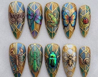 Puede incluir: Un juego de diez uñas postizas en forma de almendra con rejillas geométricas doradas estilo vitral. Cada uña muestra una criatura detallada, incluyendo una polilla, libélula, rana, mariposa, mariquita, escorpión, mantis, escarabajo, abeja y caracol.