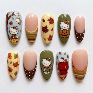 Può includere: Un set di dieci unghie finte a mandorla con motivi a tema autunnale. Le unghie presentano illustrazioni di Hello Kitty, foglie d'acero, zucche, motivi a righe e pois marroni nei toni del verde oliva, crema e blu.
