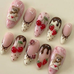 May include: A set of ten artificial nails with various designs. The nails feature a light pink base with designs including cherries, strawberries, bows, roses, chocolate drips, and a teddy bear holding an envelope. Some nails have a polka dot pattern.