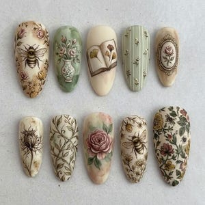 May include: A set of ten almond-shaped artificial nails with intricate floral and insect designs. The nails feature hand-painted details including roses, bees, and botanical patterns in a soft, vintage color palette. The designs include a book, a vase, and a framed rose.