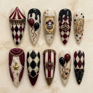 May include: A set of ten almond-shaped press-on nails featuring a circus theme with a color palette of cream, burgundy, and black. Designs include harlequin patterns, a jester card, balloons, a ticket, a sun charm, and gold star accents.