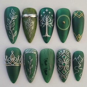 Può includere: Un set di dieci nail art verde smeraldo con vari dettagli argentati e dorati. I disegni includono foglie, un albero, uno scudo, una corona e motivi geometrici. Alcune unghie presentano piccole gemme e una catena montuosa.