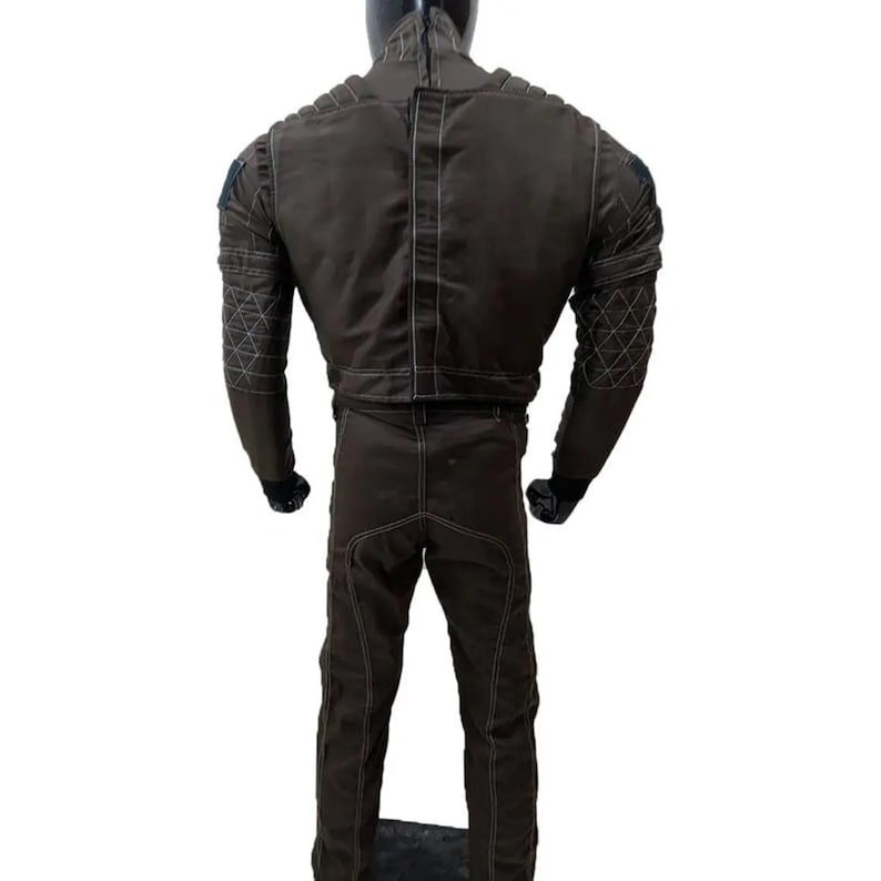 May include: A brown jumpsuit with white stitching and diamond-patterned accents on the sleeves. The suit has a high collar and is displayed on a mannequin. The back view shows the full garment.