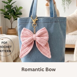 May include: A light pink crocheted bow attached to a denim tote bag with a gold-colored keychain. The bow is the focal point, with a textured, ribbed design. The words "PDF CROCHET PATTERN" are in a circle.