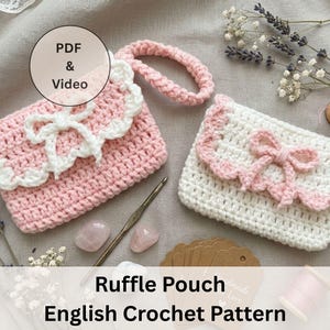 Può includere: Due pochette a volant all'uncinetto fatte a mano, una rosa e una bianca, con fiocco e finiture smerlate. Le pochette hanno un cinturino da polso e sono esposte con strumenti per uncinetto ed elementi decorativi. L'immagine include il testo "Ruffle Pouch English Crochet Pattern".