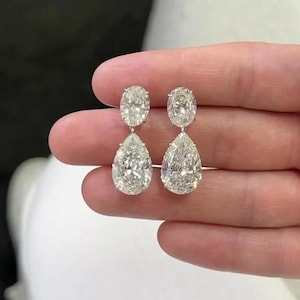 May include: A pair of drop earrings featuring a clear, faceted oval-shaped stone at the top connected to a larger, clear, faceted pear-shaped stone at the bottom. The stones are set in a silver-toned metal, creating a bright, reflective appearance.