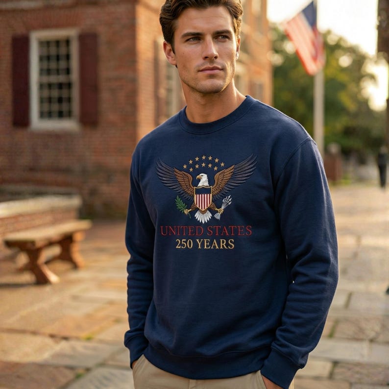 May include: Navy blue sweatshirt featuring an embroidered eagle design with the text "UNITED STATES 250 YEARS". The eagle is depicted with outstretched wings, surrounded by stars. The sweatshirt is a crew neck style.