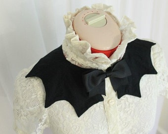 May include: A white lace blouse with a black bat-shaped collar and a black bow tie.