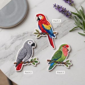 May include: Three embroidered bird patches. Patch 1 is a red, yellow, and blue macaw on a branch. Patch 2 is a gray parrot with a red tail on a branch. Patch 3 is a green and pink lovebird on a branch. Each patch has a white border.