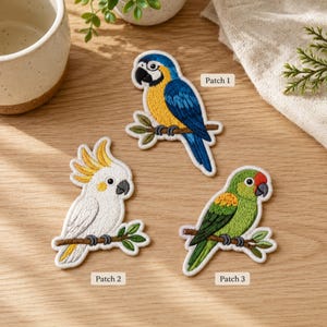 May include: Three embroidered bird patches featuring a blue and yellow macaw labeled Patch 1, a white cockatoo with a yellow crest labeled Patch 2, and a green parrot with a red forehead labeled Patch 3, each perched on a small brown branch.