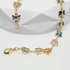 May include: Gold-toned bracelet featuring colorful butterfly charms. Each butterfly is enameled in a different color, including green, blue, yellow, orange, and purple. The bracelet has a lobster clasp closure. Text on the image reads "Pami Andr NYC".