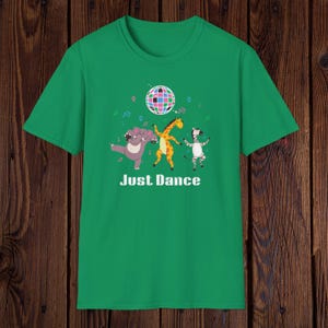 May include: Green t-shirt with a cartoon design featuring a hippo, giraffe, and zebra dancing under a disco ball. The text "Just Dance" is printed below the characters.