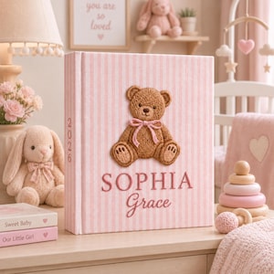May include: A light pink and white striped photo album featuring a brown embroidered teddy bear with a pink ribbon. The name SOPHIA Grace is printed in pink below the bear, and the year 2026 is vertically aligned on the spine of the album.