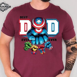 A man wearing a burgundy t-shirt with a graphic design featuring a superhero character and the text "Best Dad Ever".