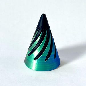 May include: A conical object featuring a metallic finish that transitions from a deep black at the pointed top to a vibrant teal and blue gradient at the base. The surface is textured with diagonal, spiraling grooves that cut into the metal.