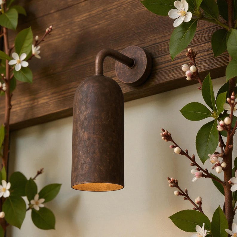 Pu&ograve; includere: Applique da parete in bronzo con paralume cilindrico e braccio curvo. L'applique &egrave; montata su una superficie in legno e circondata da rami fioriti con fiori bianchi. L'apparecchio ha una finitura strutturata.