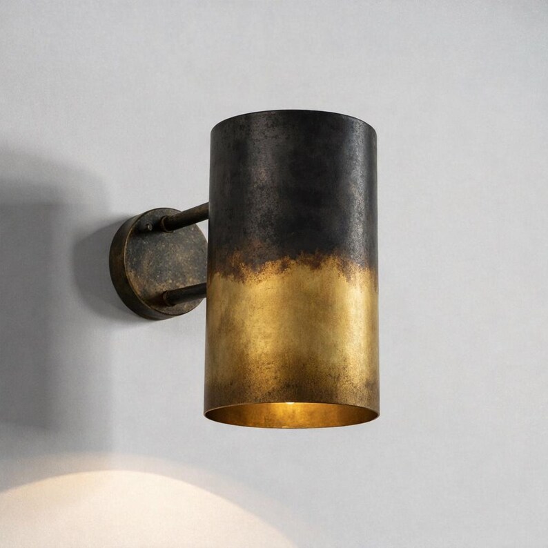 May include: A cylindrical wall sconce with a two-tone finish. The top half is dark, transitioning to a golden hue at the bottom. The sconce is mounted on a circular base with a curved arm.
