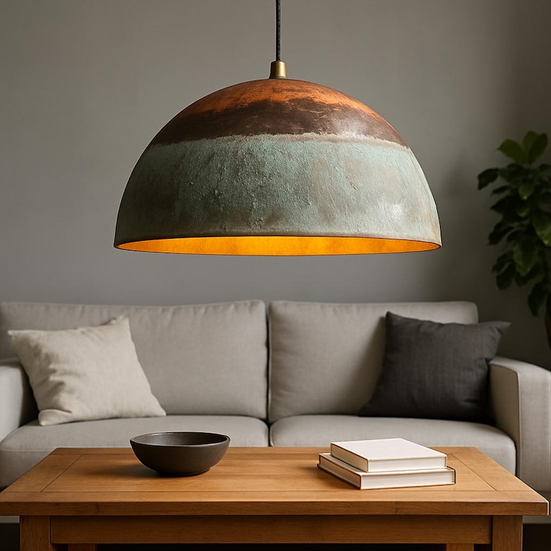 May include: A large, dome-shaped pendant light with a copper and teal finish. The interior of the light fixture has a warm, golden glow. The light hangs from a black cord and is suspended above a wooden coffee table.