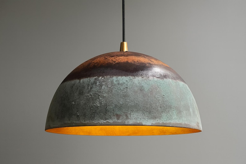 May include: A dome-shaped pendant light fixture with a textured, multi-toned surface. The top section is brown, transitioning to a dark band, then a turquoise-green lower section. The interior glows with a warm, golden light.