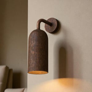 Pu&ograve; includere: Applique da parete color bronzo con paralume cilindrico e braccio curvo. L'applique &egrave; montata su una base circolare e proietta una luce calda. L'apparecchio ha una superficie strutturata e un'estetica vintage.