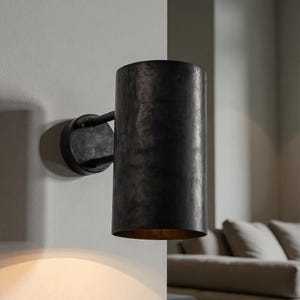 May include: A cylindrical wall sconce with a dark, textured finish. The sconce is mounted on a circular base with a curved arm. The interior of the sconce has a warm, golden glow. This fixture is suitable for indoor lighting.