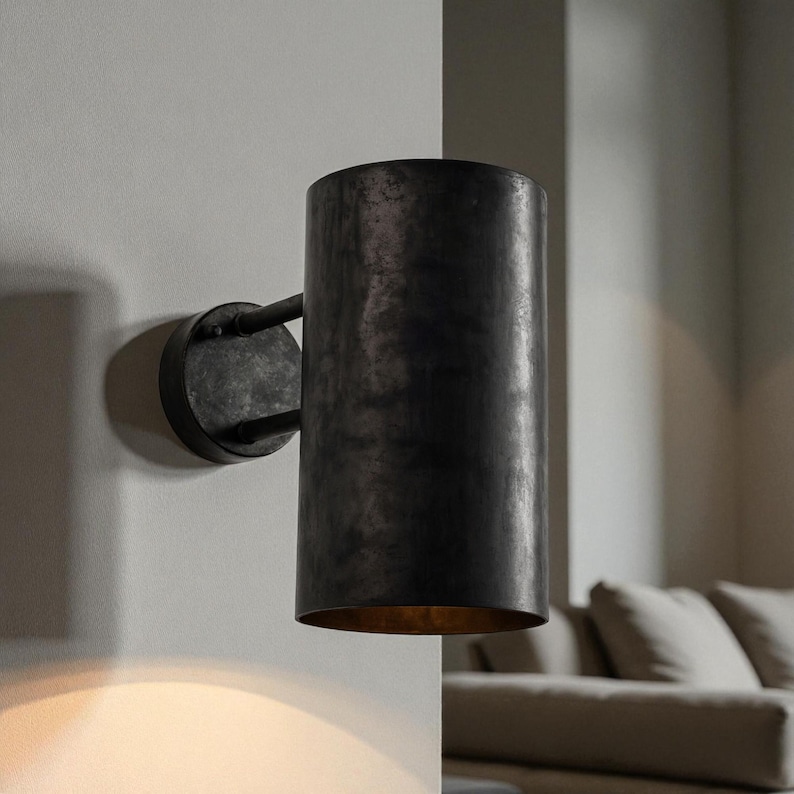 May include: A cylindrical wall sconce with a dark, textured finish. The sconce is mounted on a circular base with a curved arm. The interior of the sconce has a warm, golden glow. This fixture is suitable for indoor lighting.