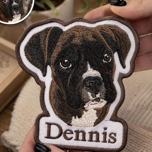 May include: A custom embroidered patch featuring a detailed portrait of a brown and black Boxer dog with a white muzzle and chest. The patch has a white border and a rectangular white tab at the bottom with the name Dennis stitched in brown.