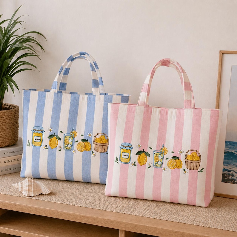 May include: Two rectangular tote bags with vertical stripes, one in light blue and white and the other in light pink and white. Both bags feature embroidered designs of a lemon jam jar, a lemon slice, a glass of lemonade, and a basket of lemons.