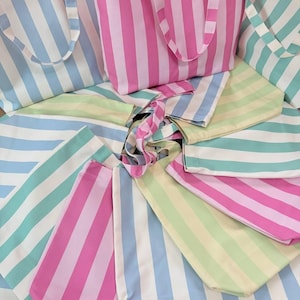 May include: A collection of multiple fabric tote bags arranged in a circular pattern. Each bag features vertical stripes in various pastel colors including pink, light blue, mint green, and pale yellow, paired with white stripes and matching handles.