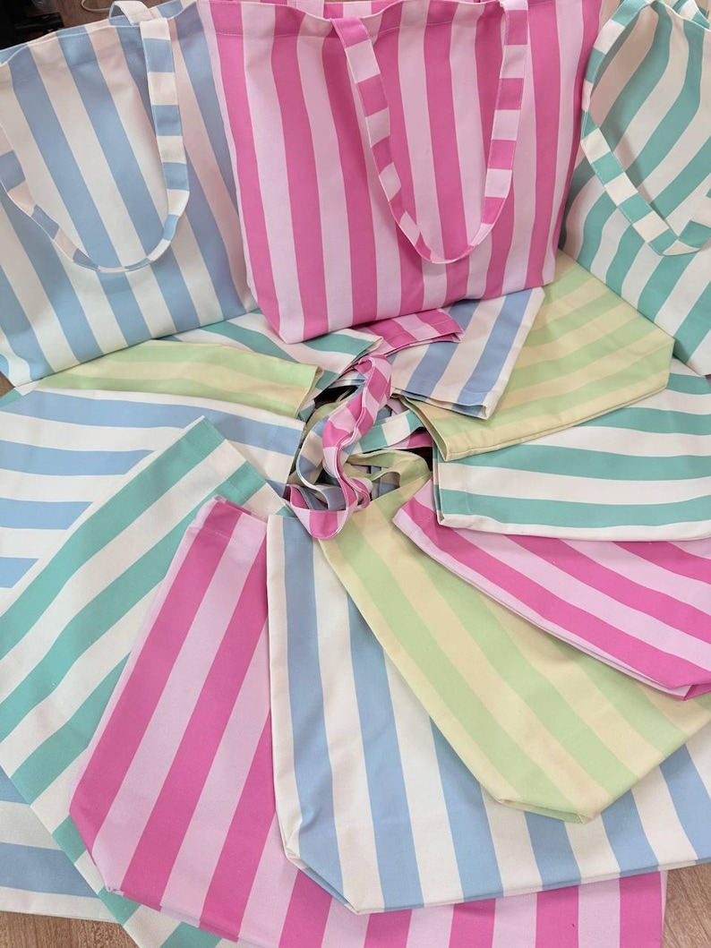 May include: A collection of multiple fabric tote bags arranged in a circular pattern. Each bag features vertical stripes in various pastel colors including pink, light blue, mint green, and pale yellow, paired with white stripes and matching handles.