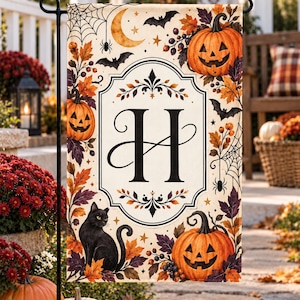May include: A rectangular garden flag featuring a central cream-coloured panel with a large black letter H. The border is decorated with orange jack-o'-lanterns, a black cat, autumn leaves, spider webs, bats, a crescent moon, and small stars.