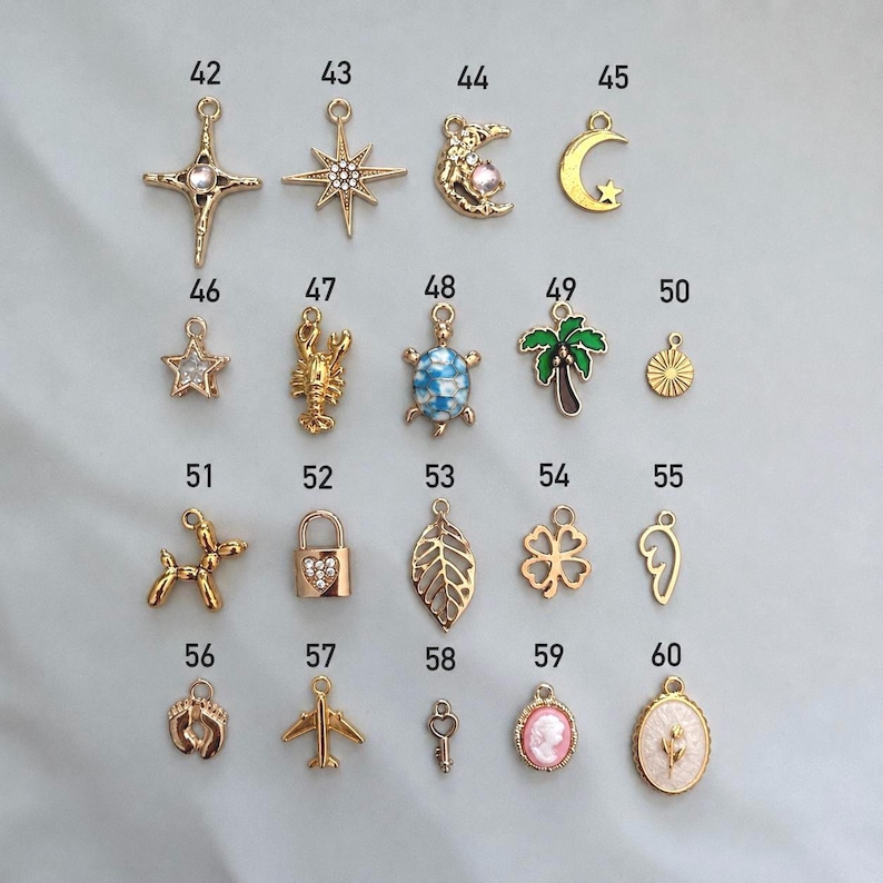 May include: A collection of gold-toned metal charms labeled 42 through 60, featuring various shapes including stars, a moon, a turtle, a palm tree, a lobster, a balloon dog, a padlock, a leaf, a clover, a wing, footprints, an airplane, and a cameo.