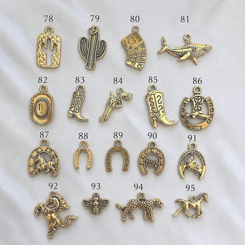 May include: A collection of gold-toned metal charms labeled 78 through 95, featuring various shapes including a cactus, playing cards, a shark, a cowboy hat, boots, a revolver, horseshoes, a horse, a bee, and a leopard, each with a jump ring.